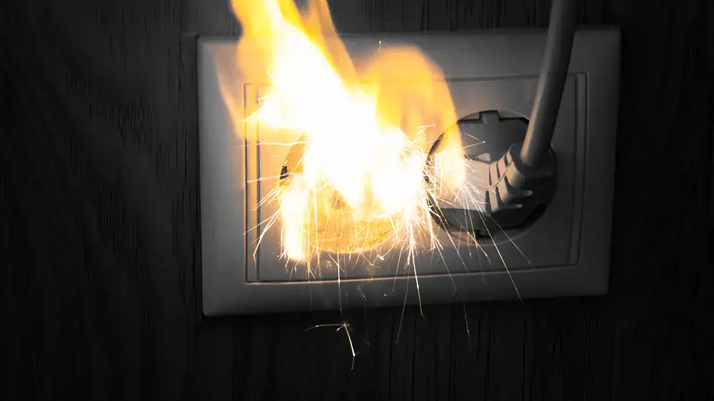 A sparking electrical outlet with a plug is on fire, showing damage that WI Water Damage Restoration fixes.