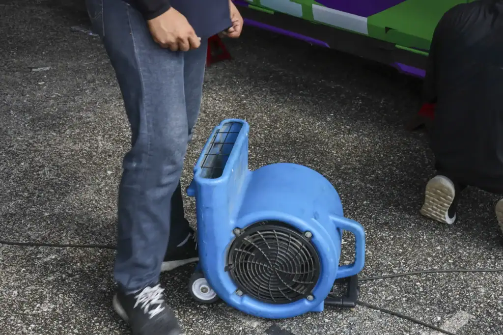 Two workers handle WI flood damage restoration, using a blue industrial floor fan and cleaning tools.