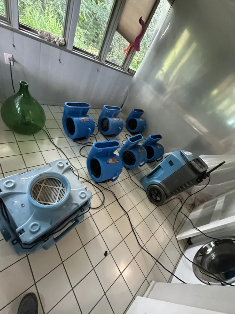 Air movers and a dehumidifier drying a tiled room after water damage