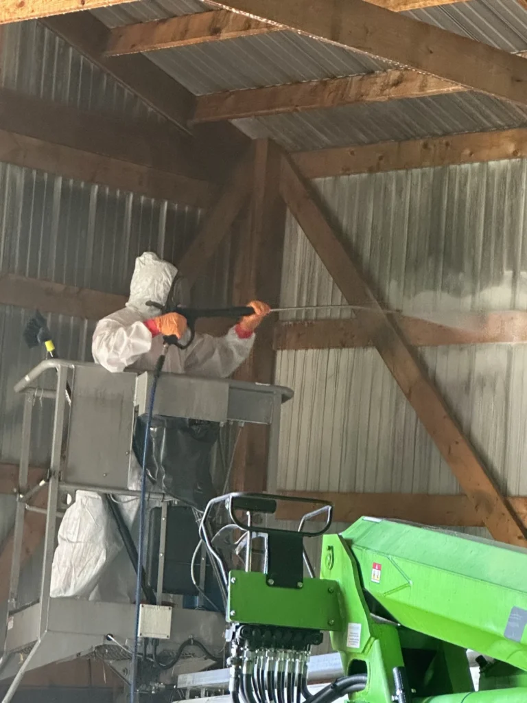 Technician in a protective suit treating roof framing from a lift during remediation