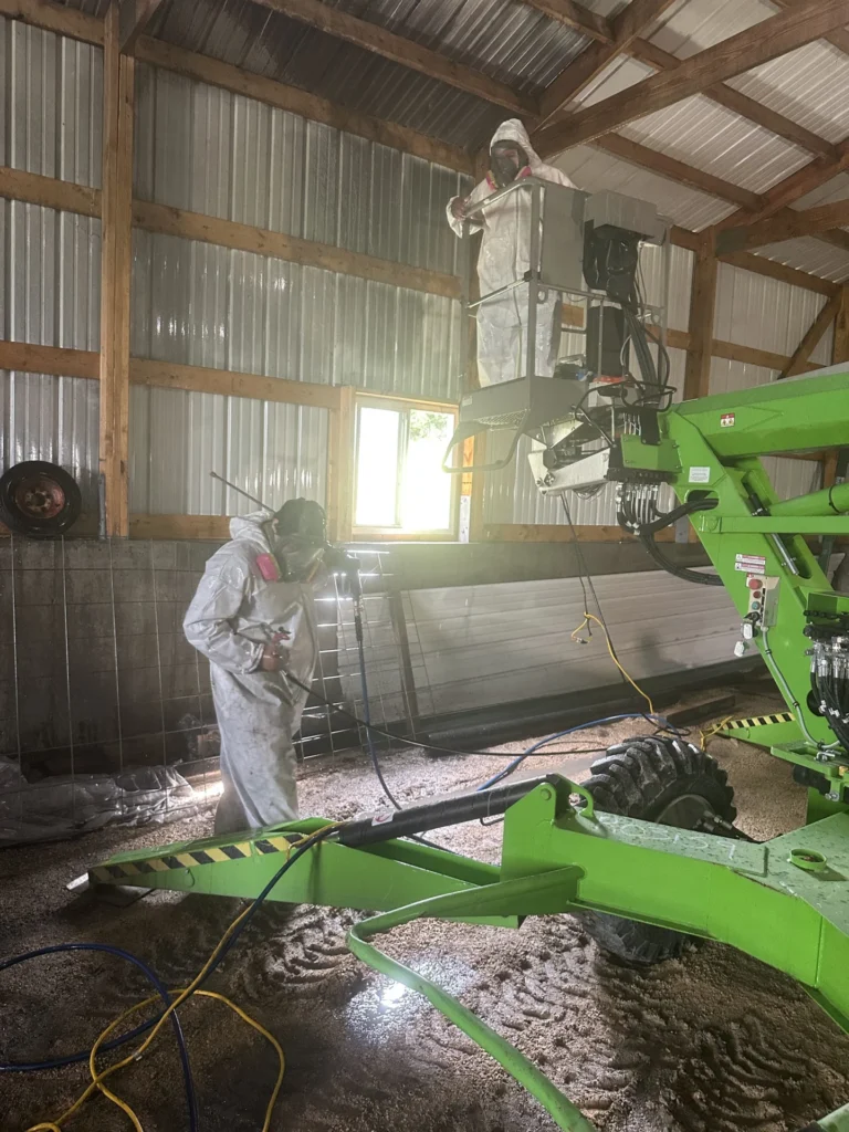 Technician in protective gear spraying exposed wood framing during remediation