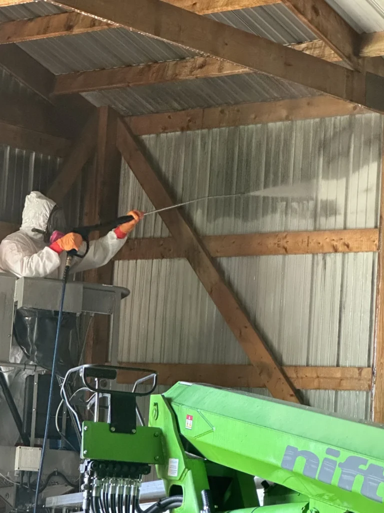 Restoration technician wearing a protective suit and respirator treating exposed rafters